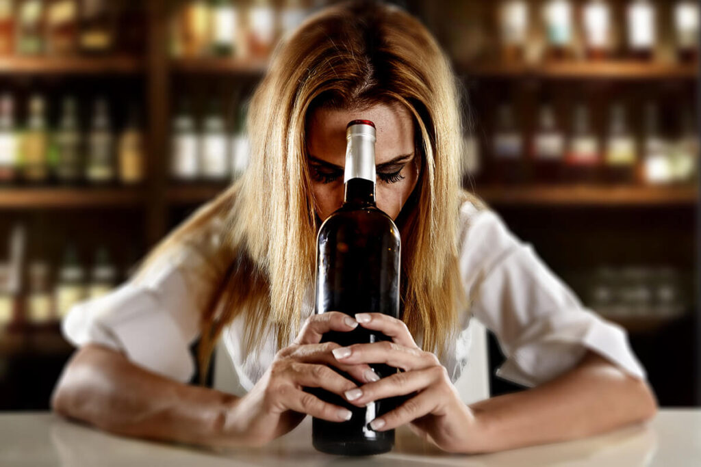 woman leaning head against liquor bottle experiencing alcohol dependence